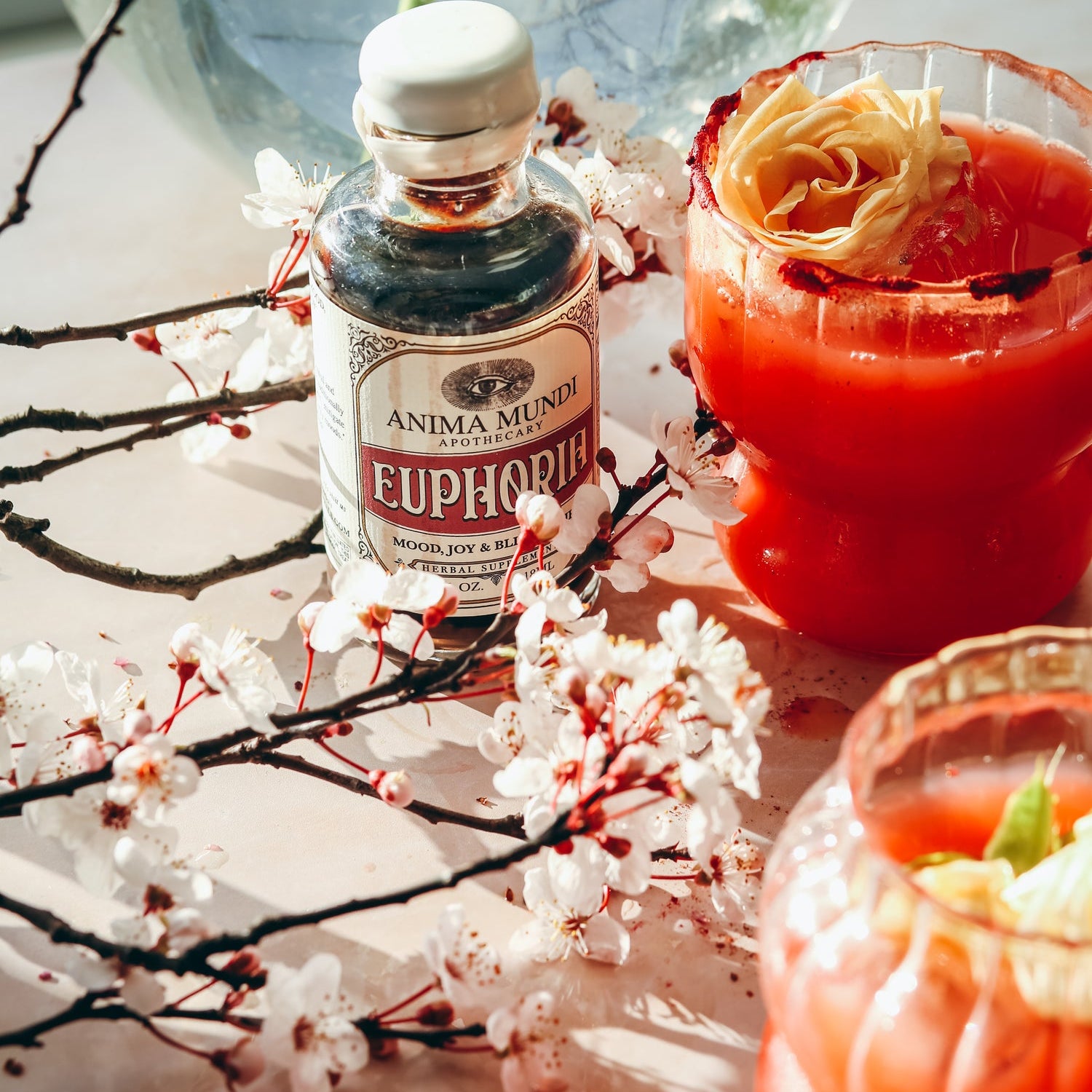Bottle of Anima Mundi Euphorica with a red cocktail and floral decorations on a light surface.