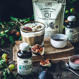 Spice blend with a glass of liquid on a wooden surface, surrounded by bottles and containers.
