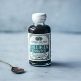 Bottle of Anima Mundi Collagen Booster on a gray surface with a spoon containing a dark liquid.