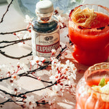 EUPHORIA Elixir bottle surrounded by blossoms and vibrant drinks, showcasing sensory vitality and energy.