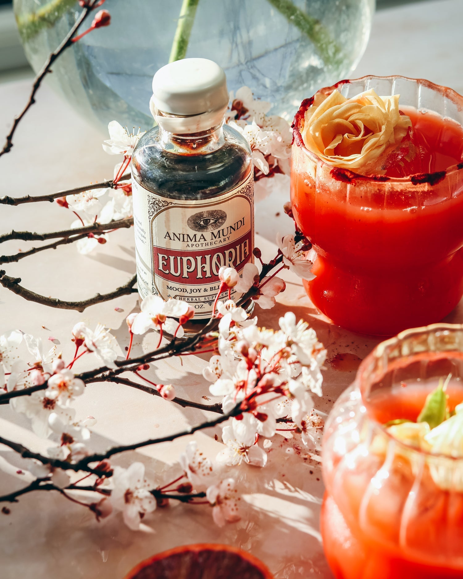 EUPHORIA Elixir bottle surrounded by blossoms and vibrant drinks, showcasing sensory vitality and energy.