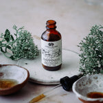 Bottle labeled 'Happiness' with dropper on a marble surface with plants