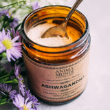 Jar of Ashwagandha powder with a spoon, surrounded by flowers on a light background