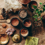 Assorted organic mushroom powders including CHAGA on a wooden table surrounded by crystals and plants.