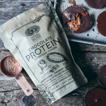 Chocolate Protein superfood powder package with powder scoop and chocolate cups.