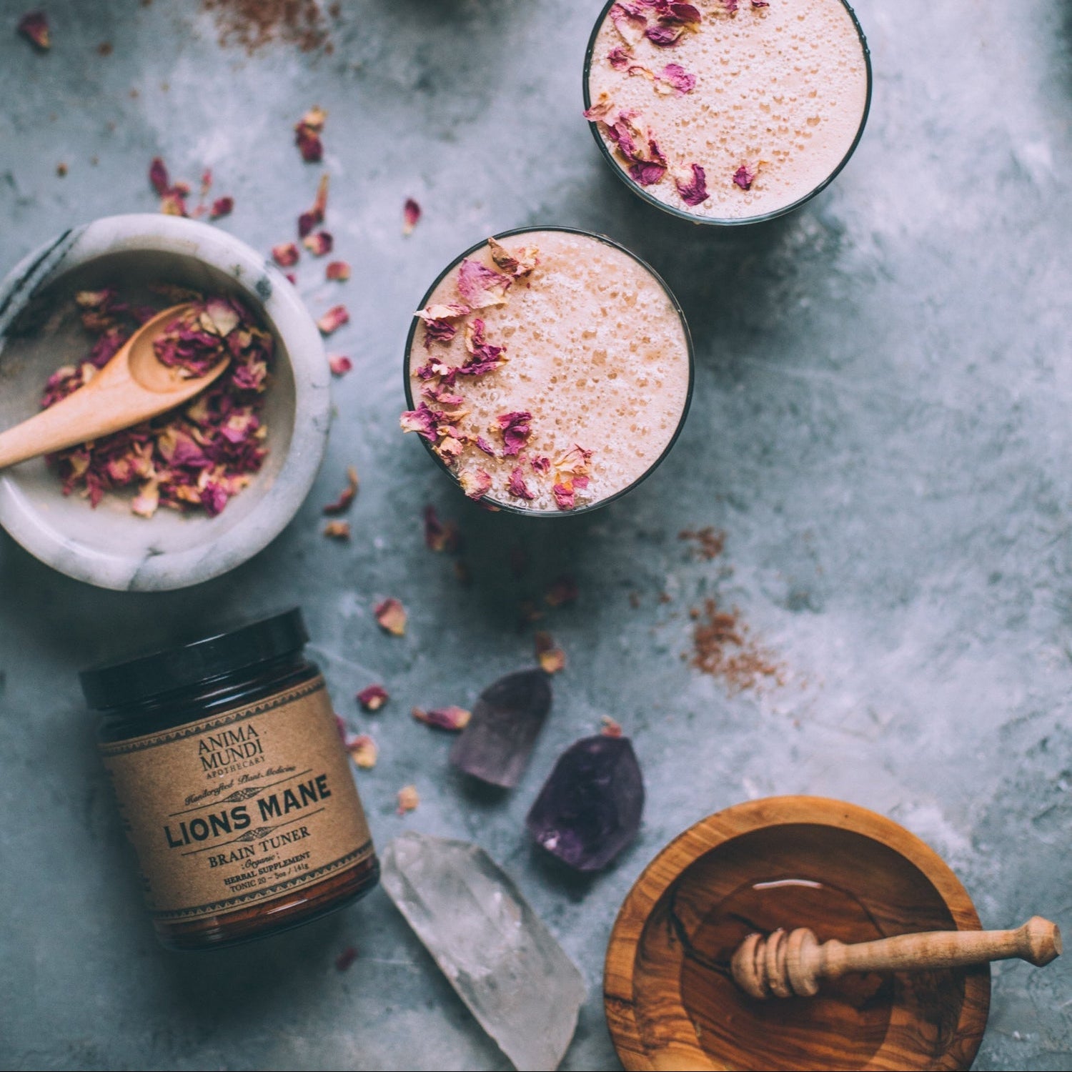 LION'S MANE organic mushroom powder beside floral-infused drinks on a rustic surface with crystals.