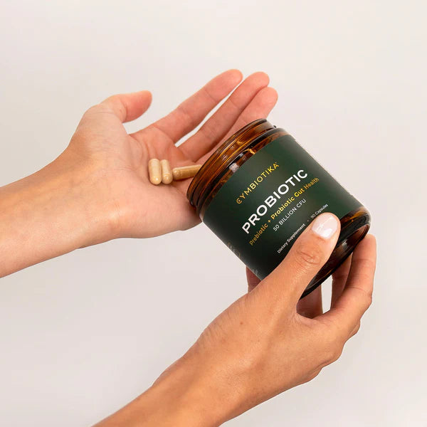 Person holding Cymbiotika Probiotic jar with capsules in hand, emphasizing daily gut health supplement.
