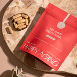 Red package labeled 'Happy Aging' with capsules on a stone surface