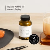 NOVOS Boost (NMN) supplement bottle on table with food and drink, impacts 7 of 12 causes of aging.