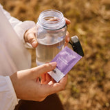 Person holding a pack of Sodii - Everyday Hydration Salts next to a water bottle outdoors.